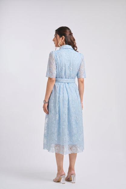 A woman viewed from the back wearing a light blue lace midi dress with short sleeves, a collar, and a matching waist tie, paired with clear high-heeled sandals against a light gray studio background.