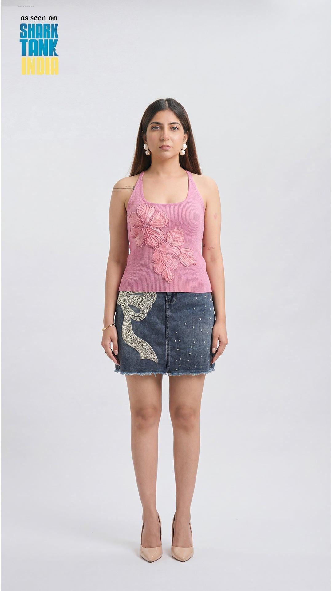 Woman wearing a pink tank top with floral design and denim skirt on a white background
