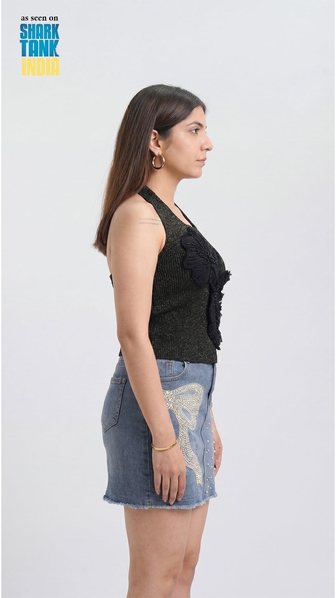 Woman wearing a black sleeveless top and denim skirt on a white background with 'Shark Tank India' branding.