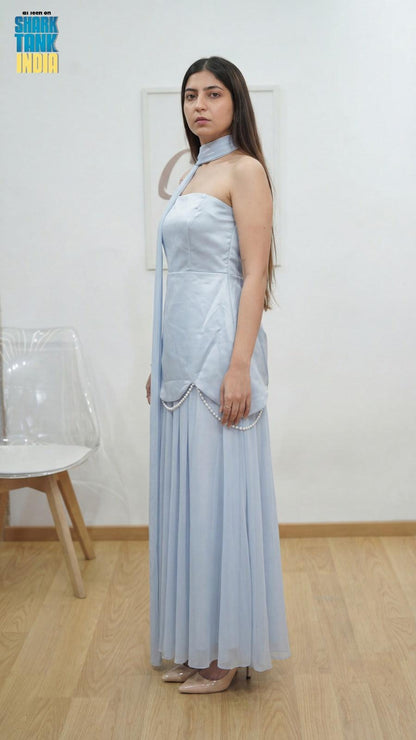 Woman wearing a light blue dress standing against a white wall.