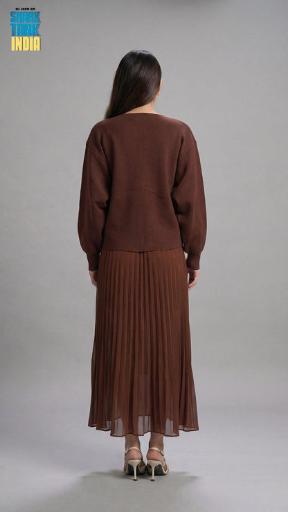 Woman wearing a brown outfit with a pleated skirt on a gray background