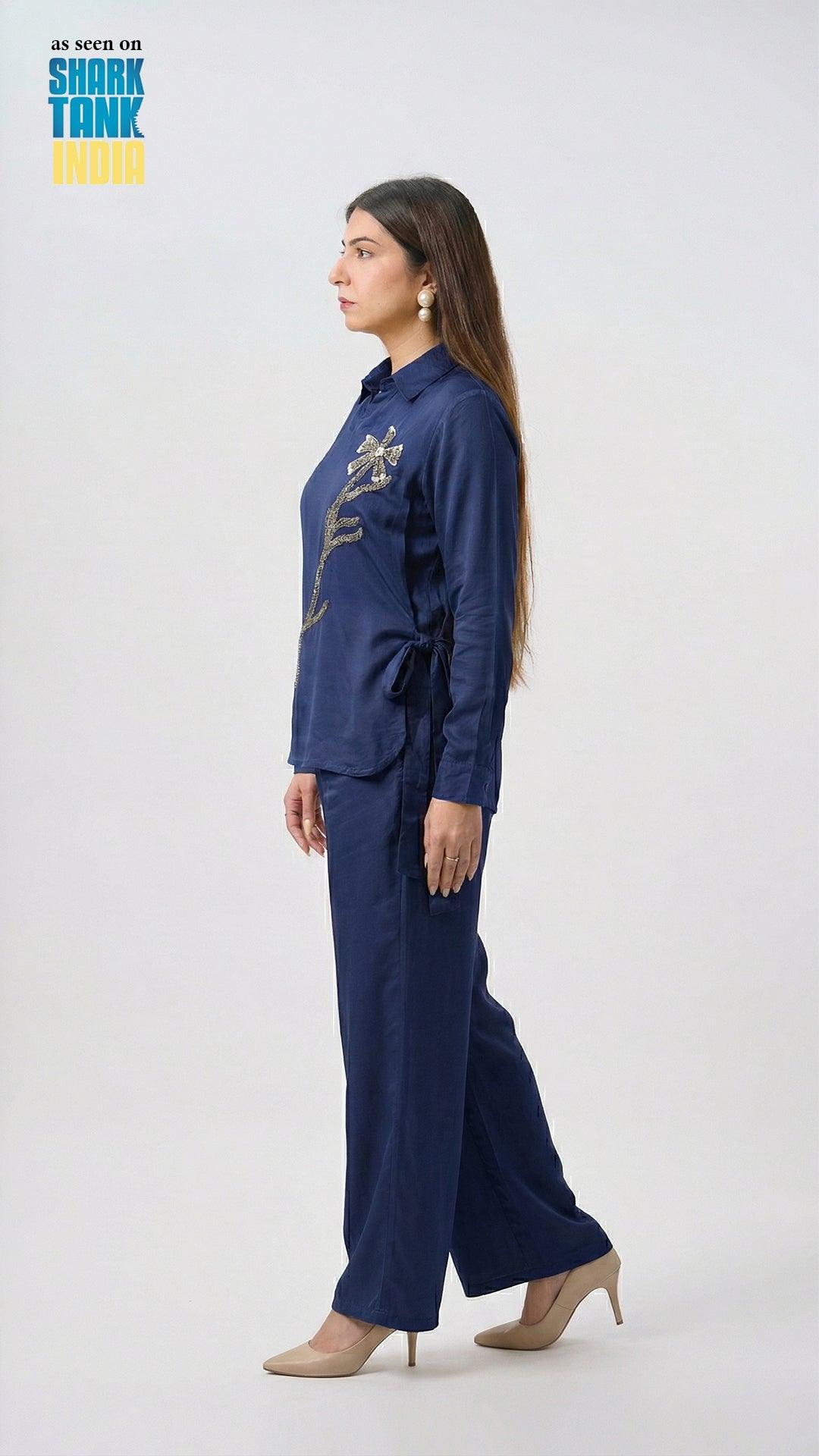 Woman wearing a navy blue outfit with a patterned shirt and wide-leg pants on a white background.