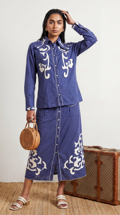 Woman wearing a blue outfit with white patterns, standing next to a vintage suitcase.
