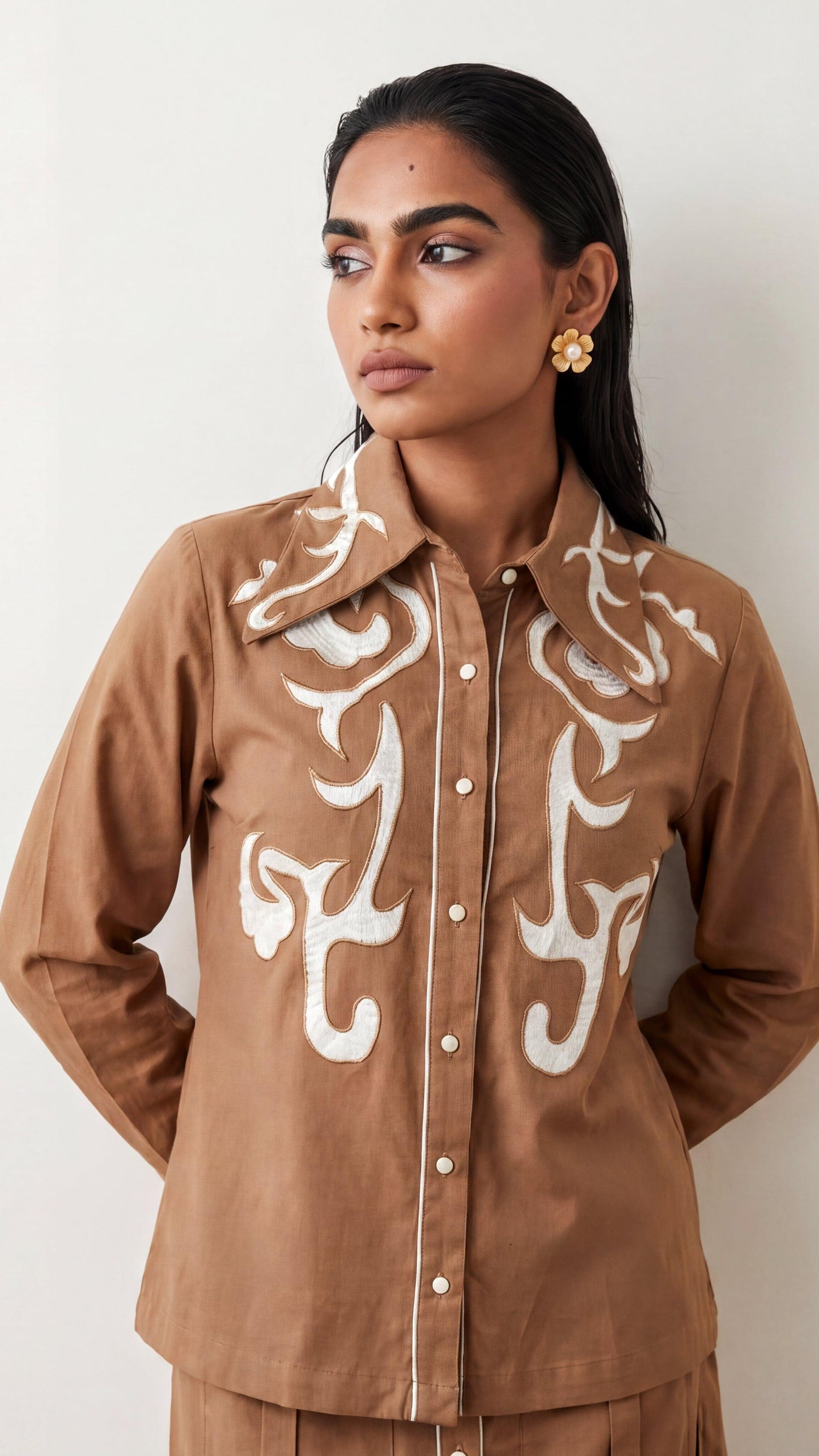 Woman wearing a brown jacket with white patterns against a plain background