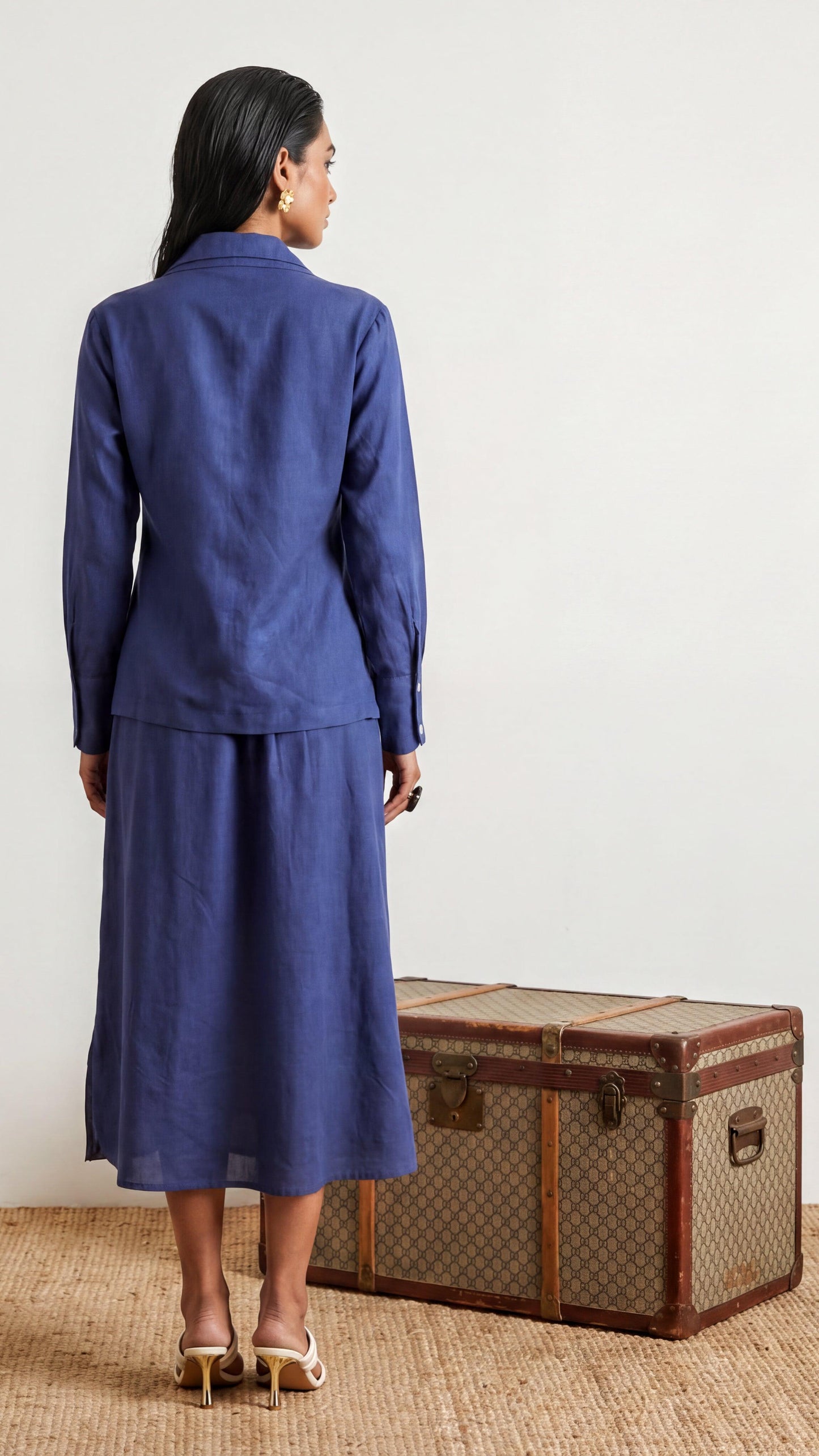 Woman in a blue suit standing next to a vintage suitcase on a light background