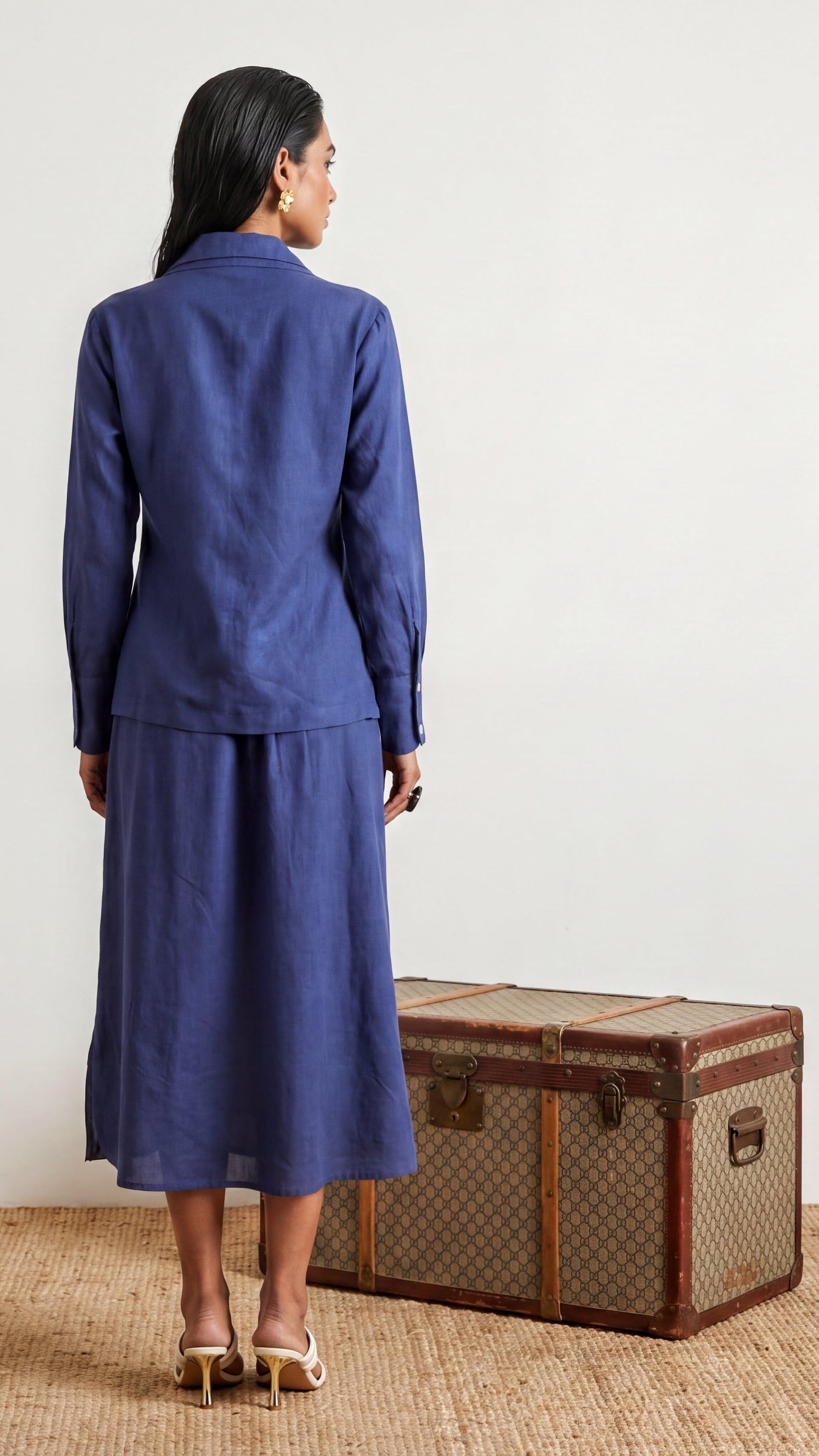 Woman in a blue suit standing next to a vintage suitcase on a light background