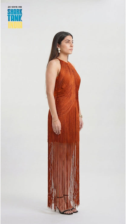 Woman wearing a rust-colored halter neck dress with fringe details on a white background, featuring Shark Tank branding.