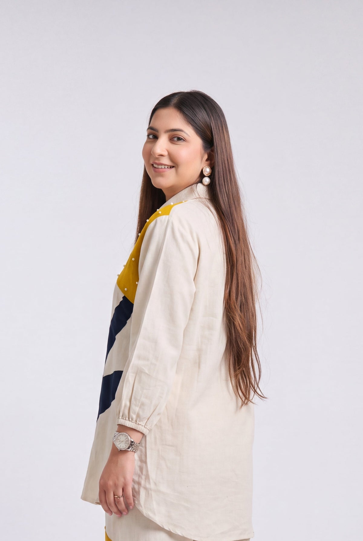A woman modeling a matching cream-colored two-piece set consisting of a long-sleeve kurta and wide-leg trousers, featuring abstract yellow and navy blue graphic panels on the back.