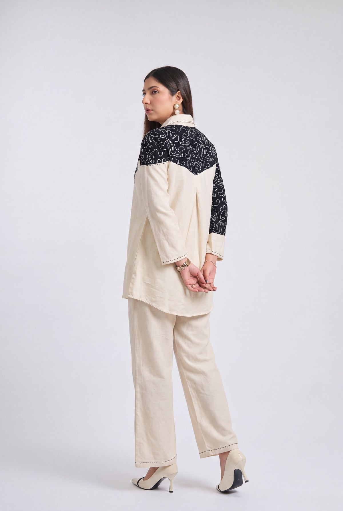 A woman modeling a two-piece cream-colored outfit with black patterned yoke panels on a light gray studio background.