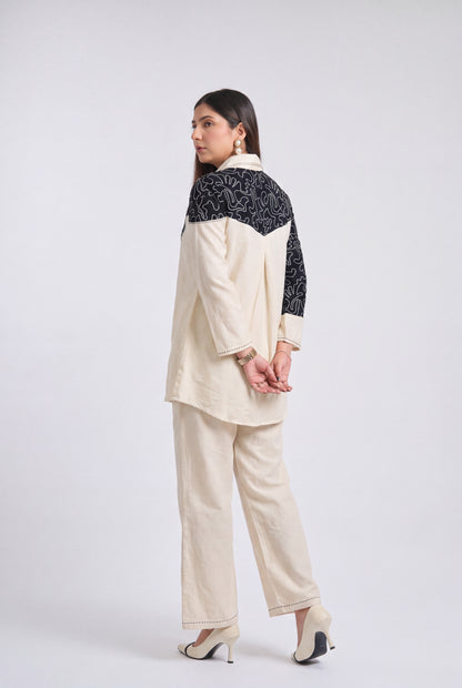 A woman modeling a two-piece cream-colored outfit with black patterned yoke panels on a light gray studio background.