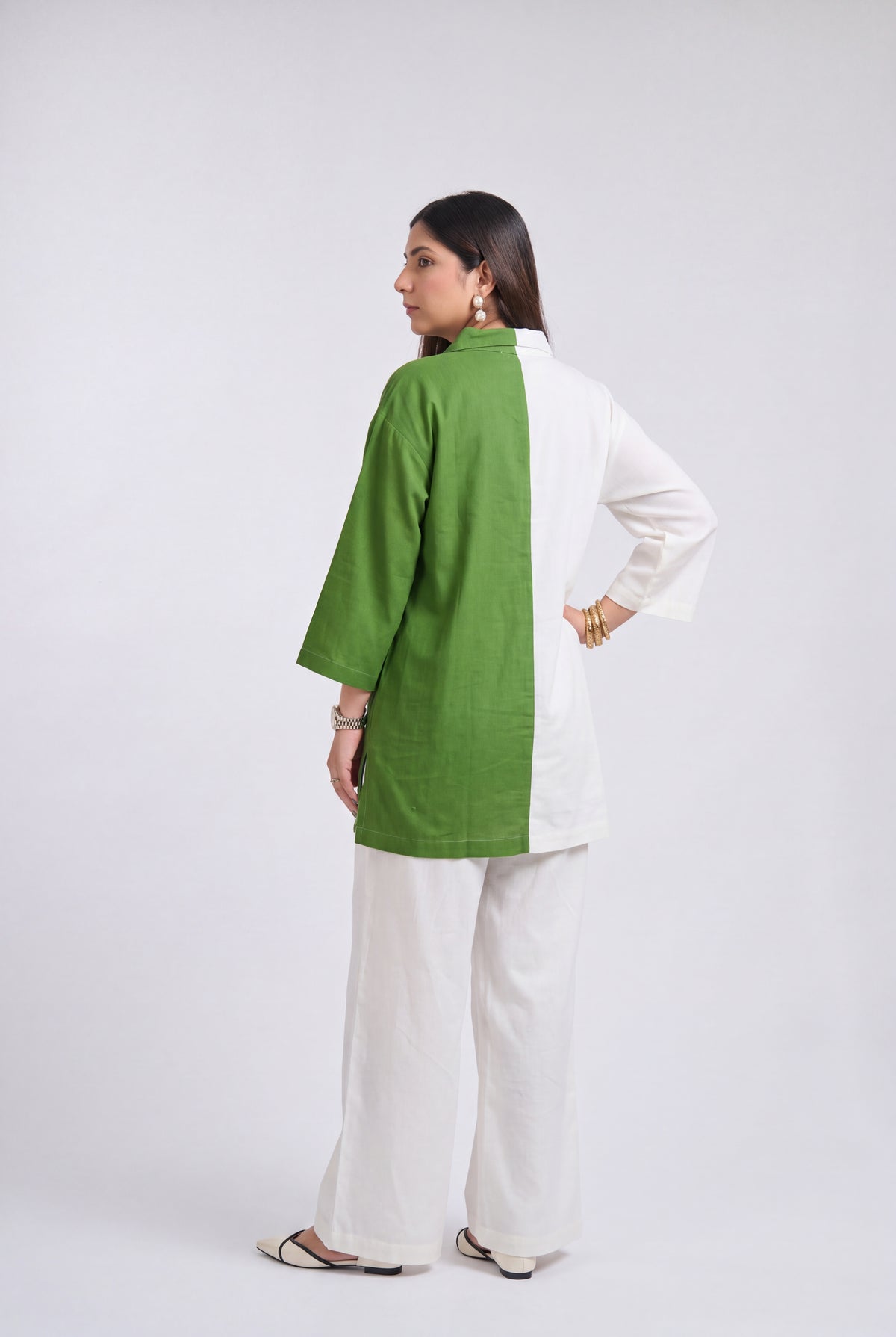 A woman modeling a two-tone green and white kurta with matching white wide-leg pants, shown from a side-back angle against a plain light gray studio background.