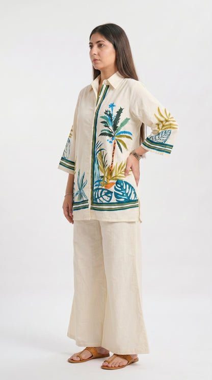Woman wearing a cream-colored outfit with tropical leaf patterns on a white background