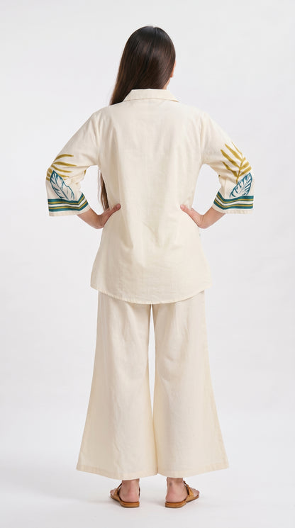 Woman wearing a beige outfit with embroidered sleeves on a white background