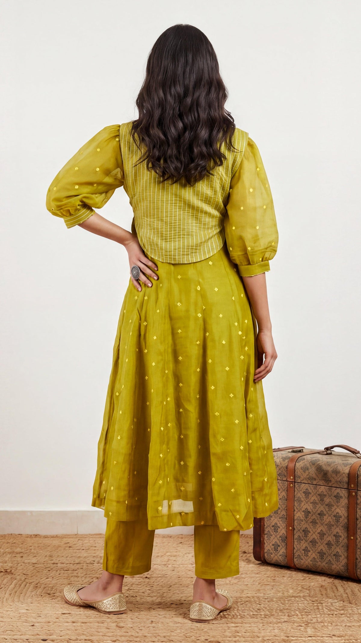 Woman wearing a yellow dress with a vintage suitcase on a wooden floor.