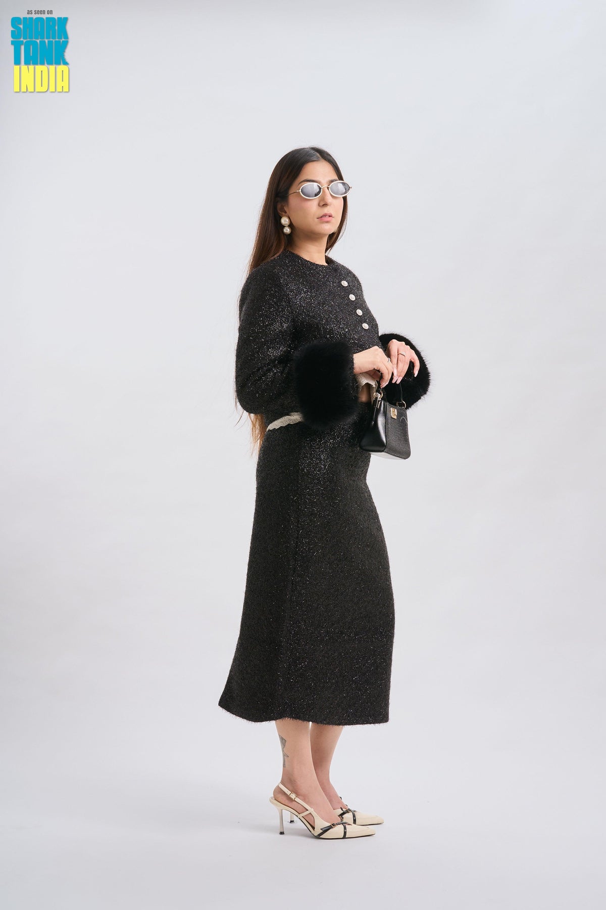 Woman in a black outfit with a skirt and jacket holding a handbag on a white background