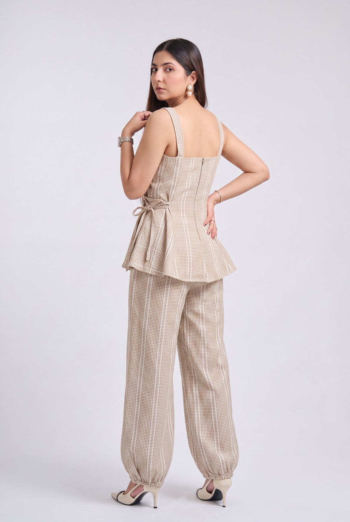 A woman modeling a beige sleeveless top and matching wide-leg trousers set with thin vertical stripes, shown from a back-three-quarter angle against a light gray studio background.