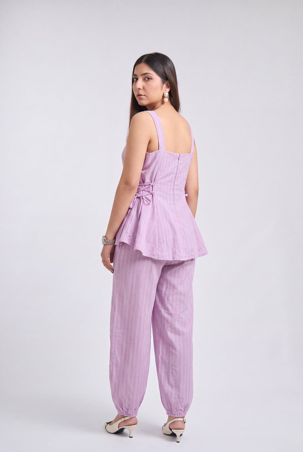 A woman modeling a light purple/lavender two-piece set consisting of a sleeveless peplum-style top and matching wide-leg pants, shown from the back against a plain light gray studio background.