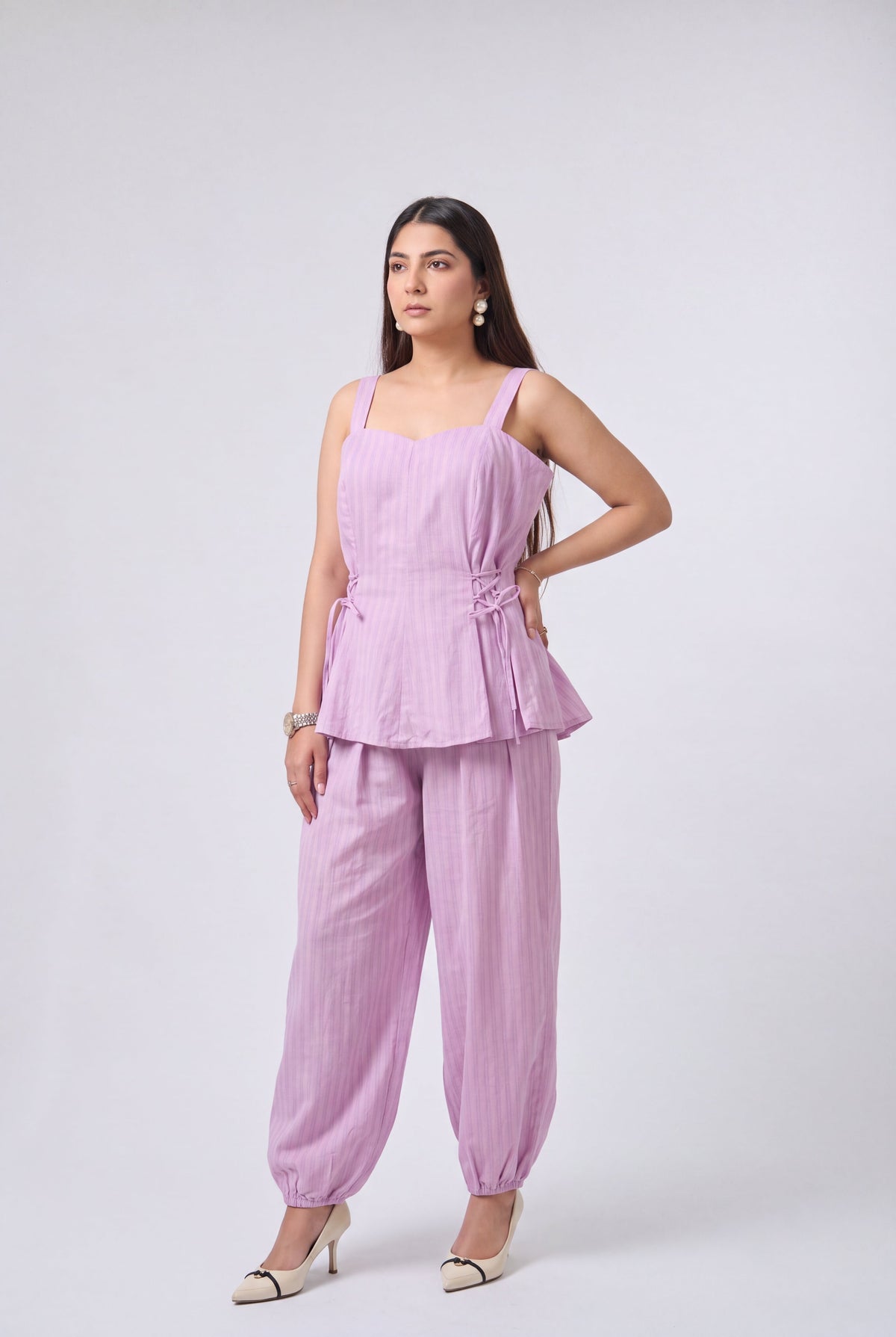 A woman modeling a light blue and white vertically striped two-piece set consisting of a sleeveless peplum top and matching wide-leg pants, paired with beige high heels against a light gray studio background.