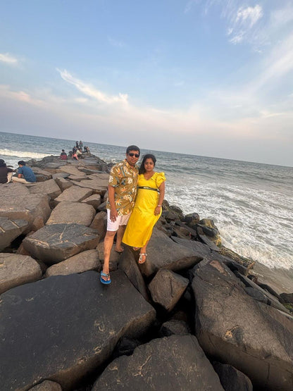 Two people standing on a rocky jetty by the ocean with a clear sky.