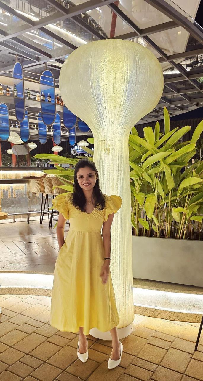 Woman in a yellow dress standing next to a large decorative light fixture in an indoor setting.