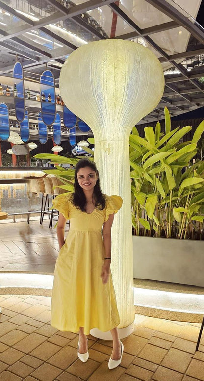 Woman in a yellow dress standing next to a large decorative light fixture in an indoor setting.