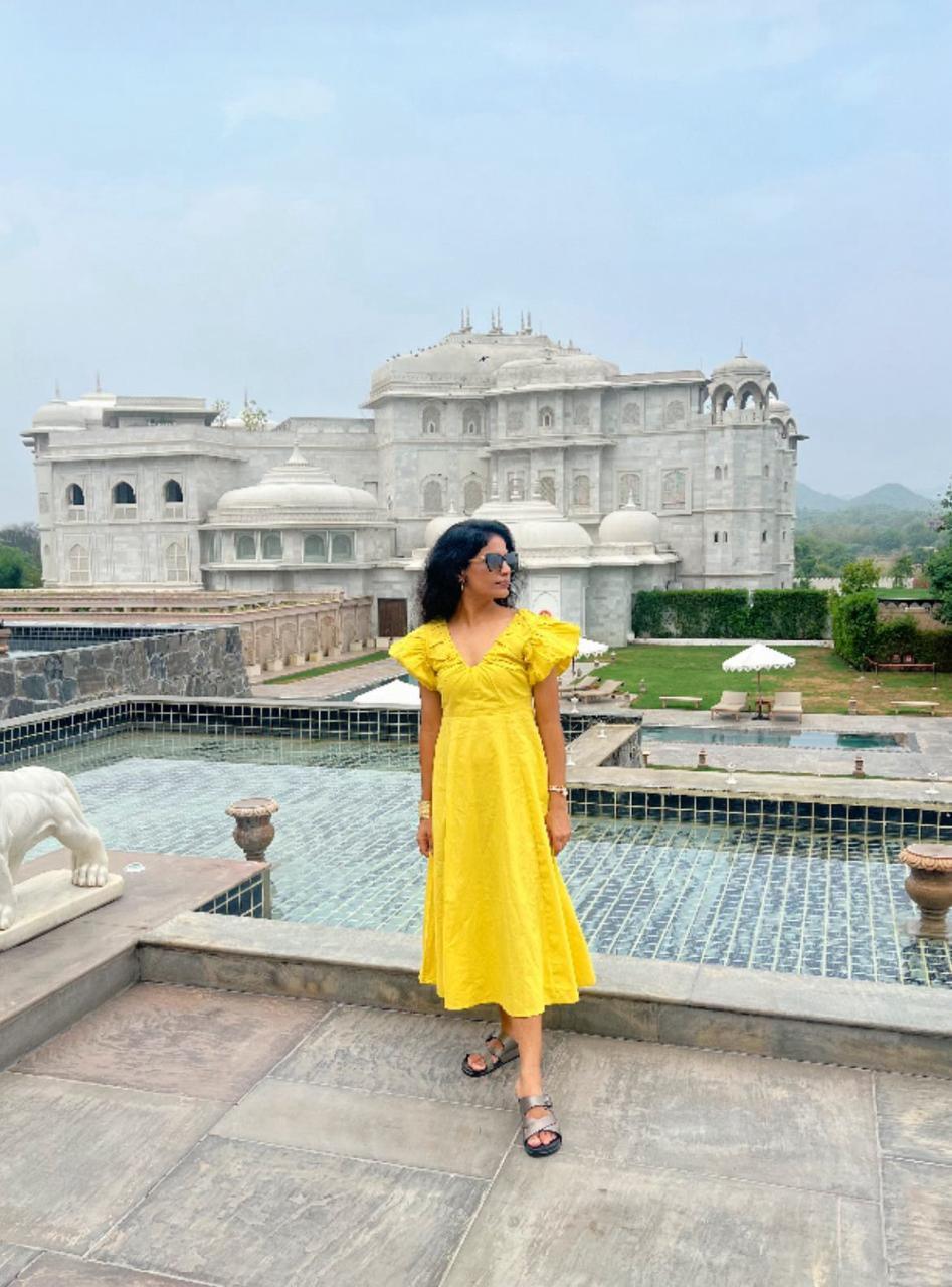 Woman in a yellow dress standing in front of a large building with a pool.