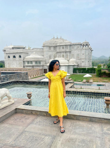 Woman in a yellow dress standing in front of a large building with a pool.