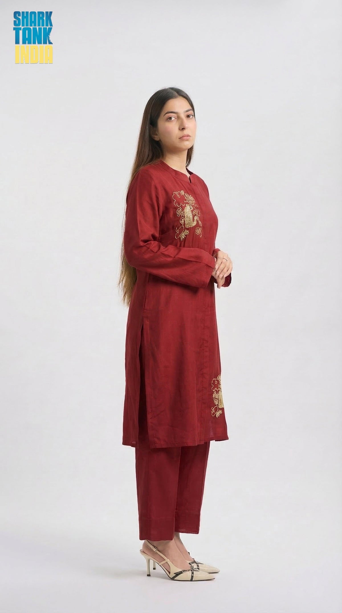 Woman wearing a maroon traditional outfit with gold embroidery on a white background