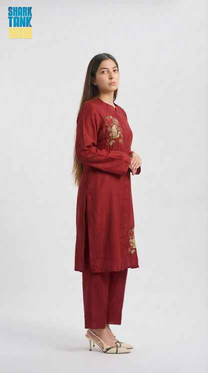 Woman wearing a maroon traditional outfit with gold embroidery on a white background