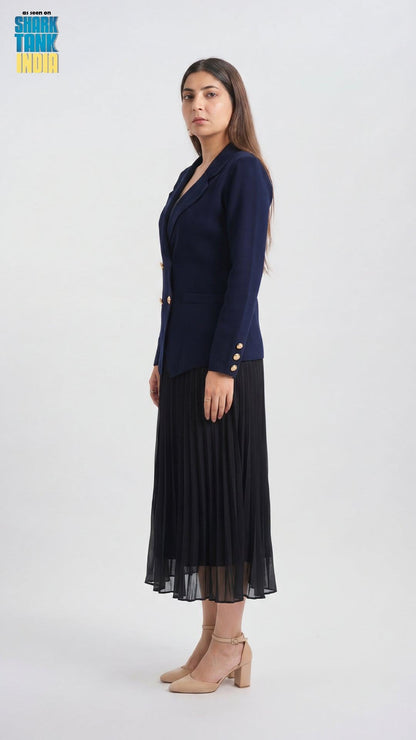 Woman wearing a navy blazer and black pleated skirt on a white background