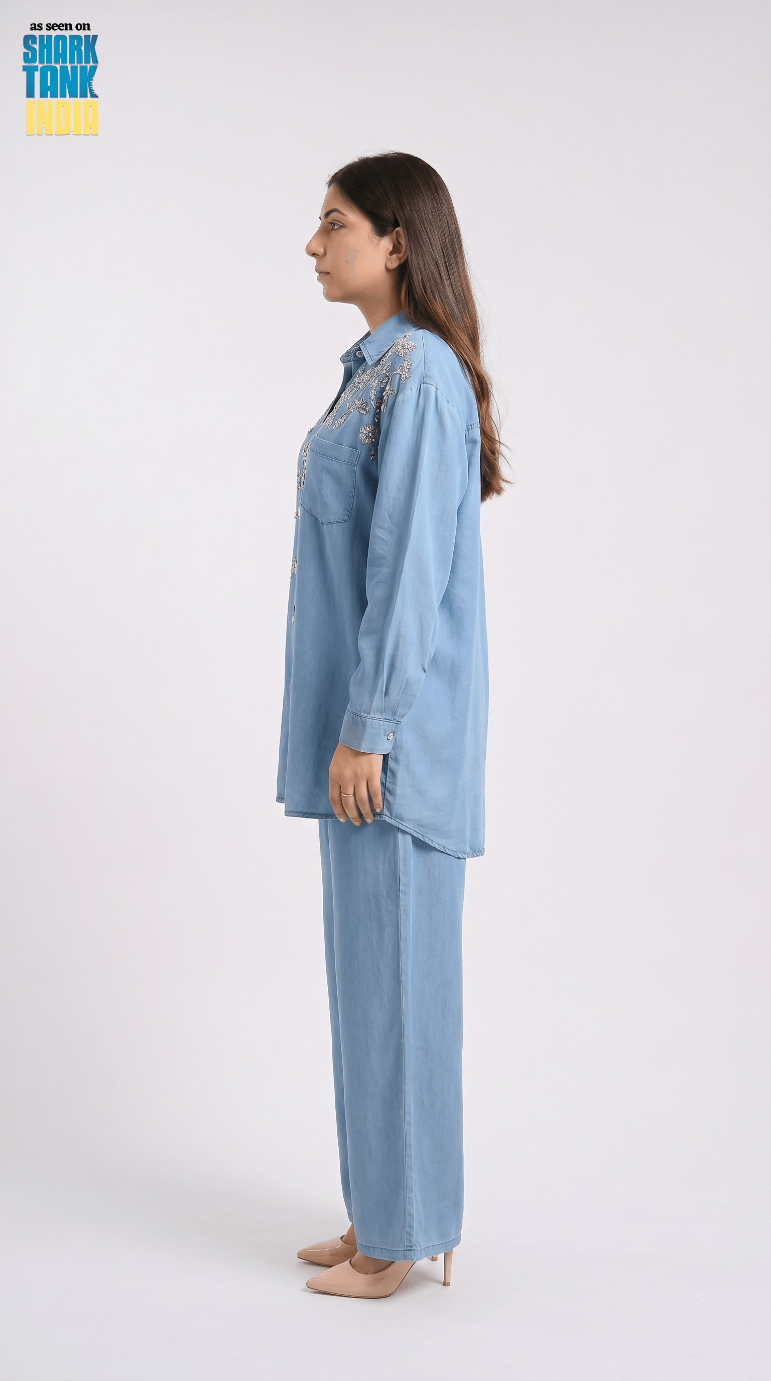 Woman wearing a light blue denim outfit with embroidery on a white background