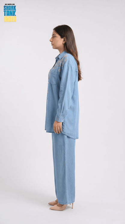 Woman wearing a light blue denim outfit with embroidery on a white background