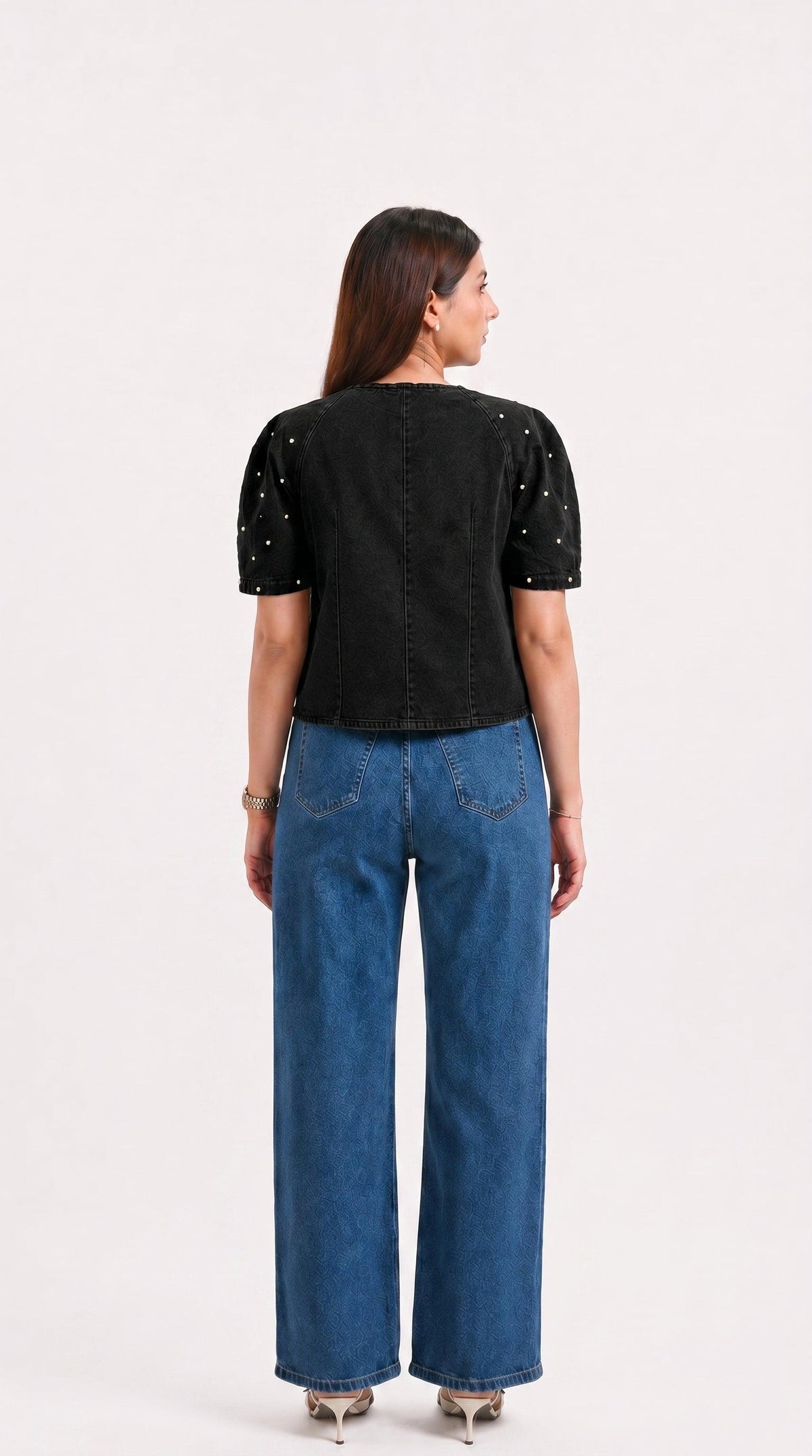 Woman wearing a black top with sequins and blue jeans on a white background