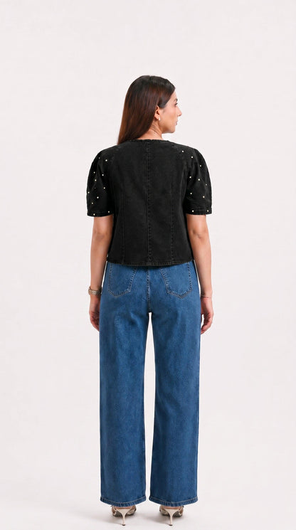 Woman wearing a black top with sequins and blue jeans on a white background