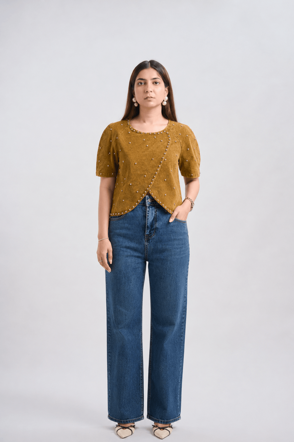 Woman wearing a mustard yellow top and blue jeans on a white background