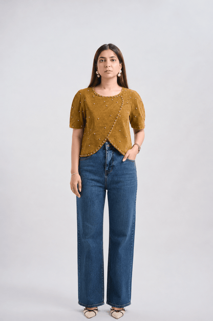 Woman wearing a mustard yellow top and blue jeans on a white background
