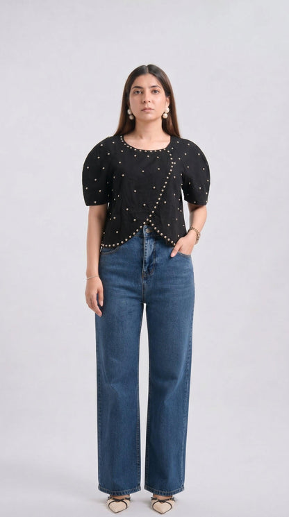 Woman wearing a black top with bead details and blue jeans on a white background