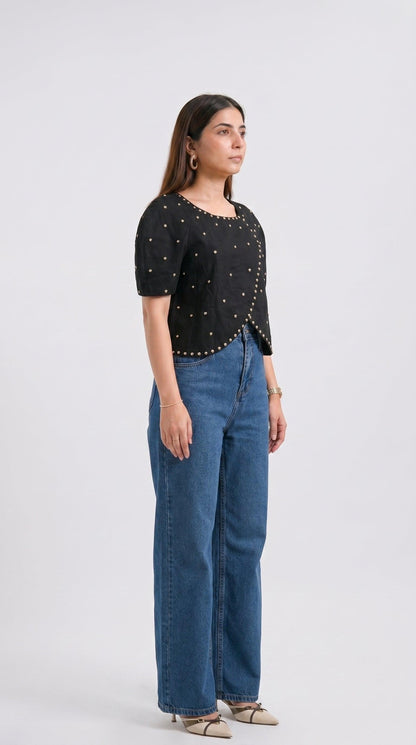 Woman wearing a black studded top and blue jeans on a white background