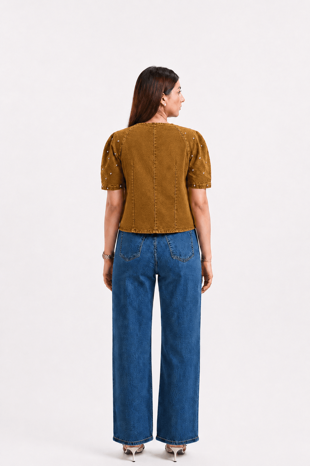 Woman wearing a mustard yellow top and blue jeans on a white background