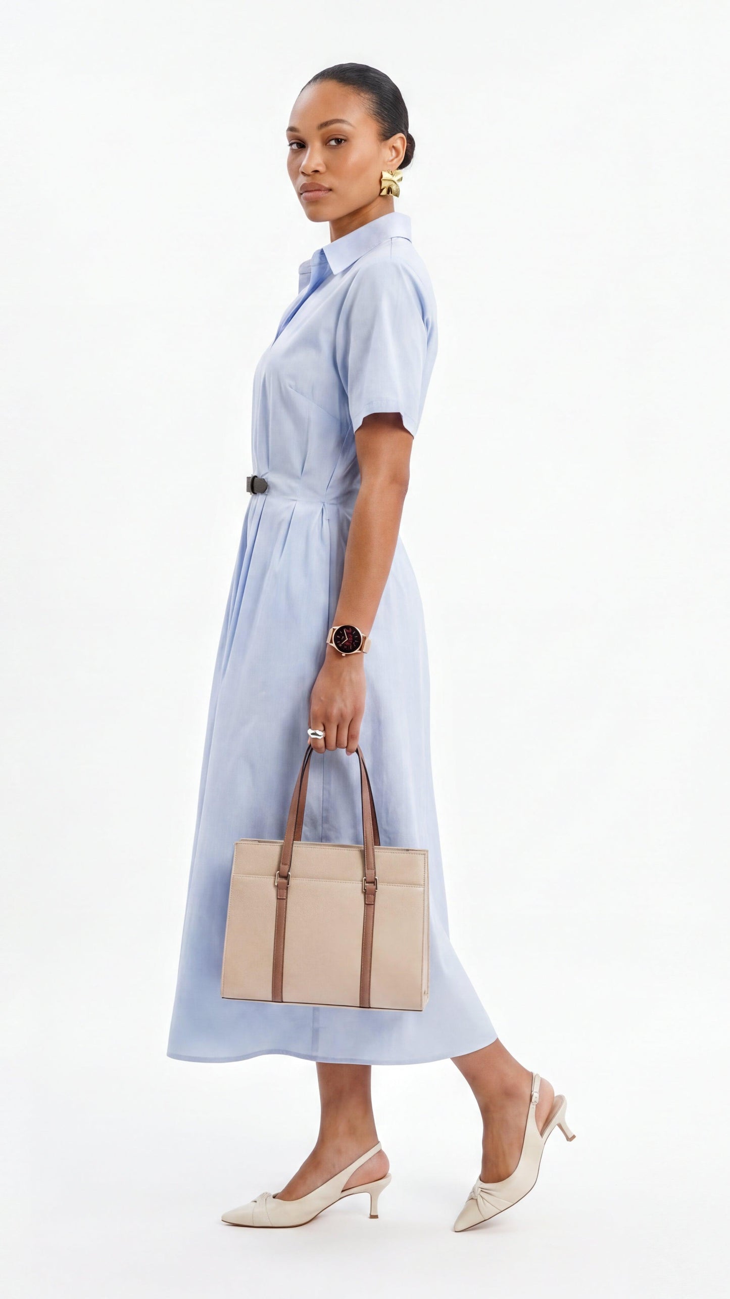 Woman wearing a light blue dress holding a beige handbag on a white background