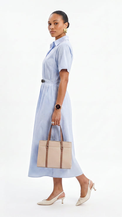 Woman wearing a light blue dress holding a beige handbag on a white background