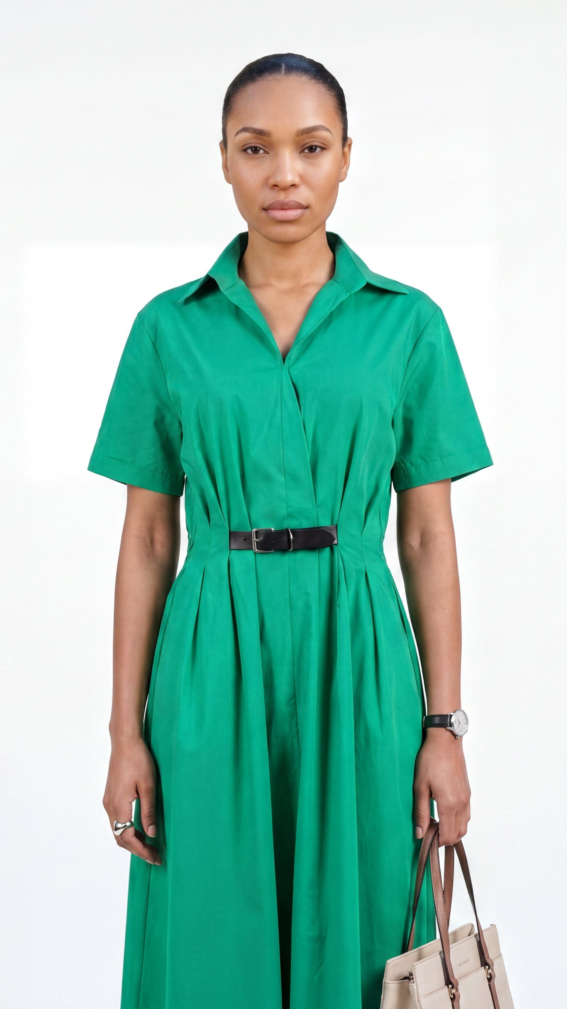 Woman wearing a green dress with a belt, holding a beige handbag on a white background