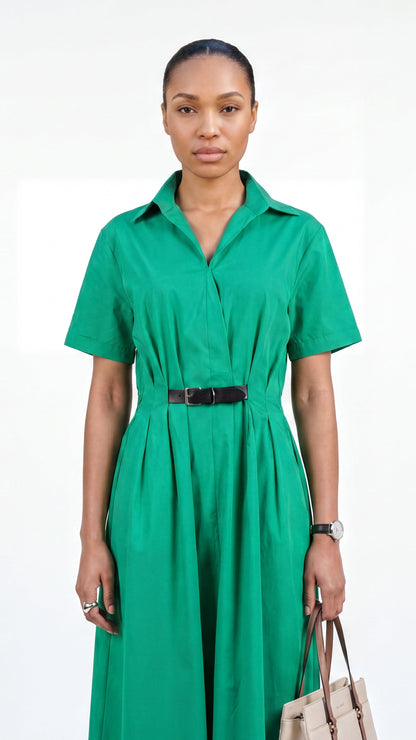Woman wearing a green dress with a belt, holding a beige handbag on a white background