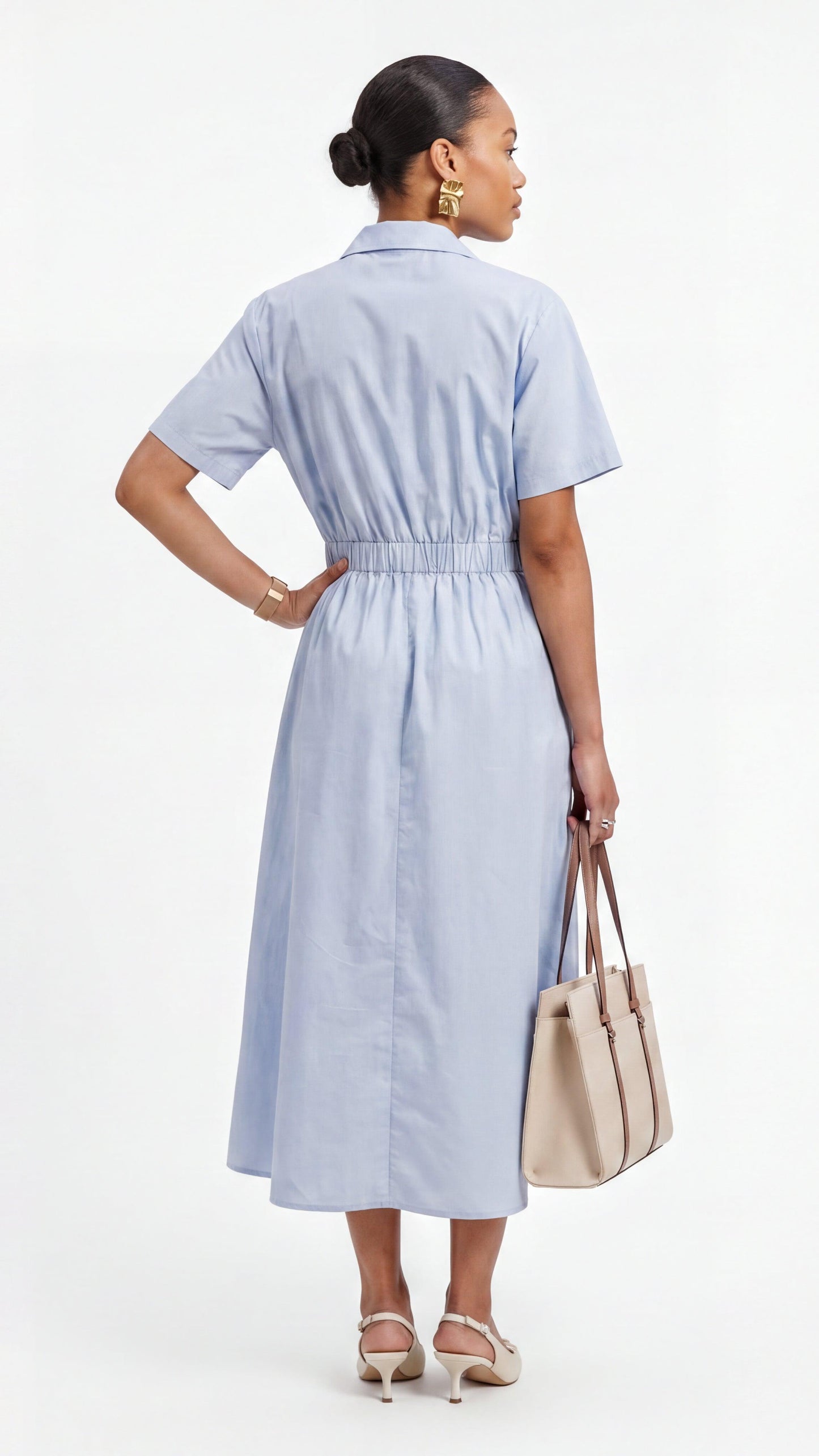Woman wearing a light blue dress holding a beige handbag on a white background