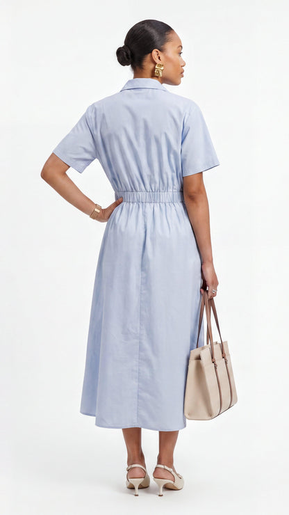 Woman wearing a light blue dress holding a beige handbag on a white background