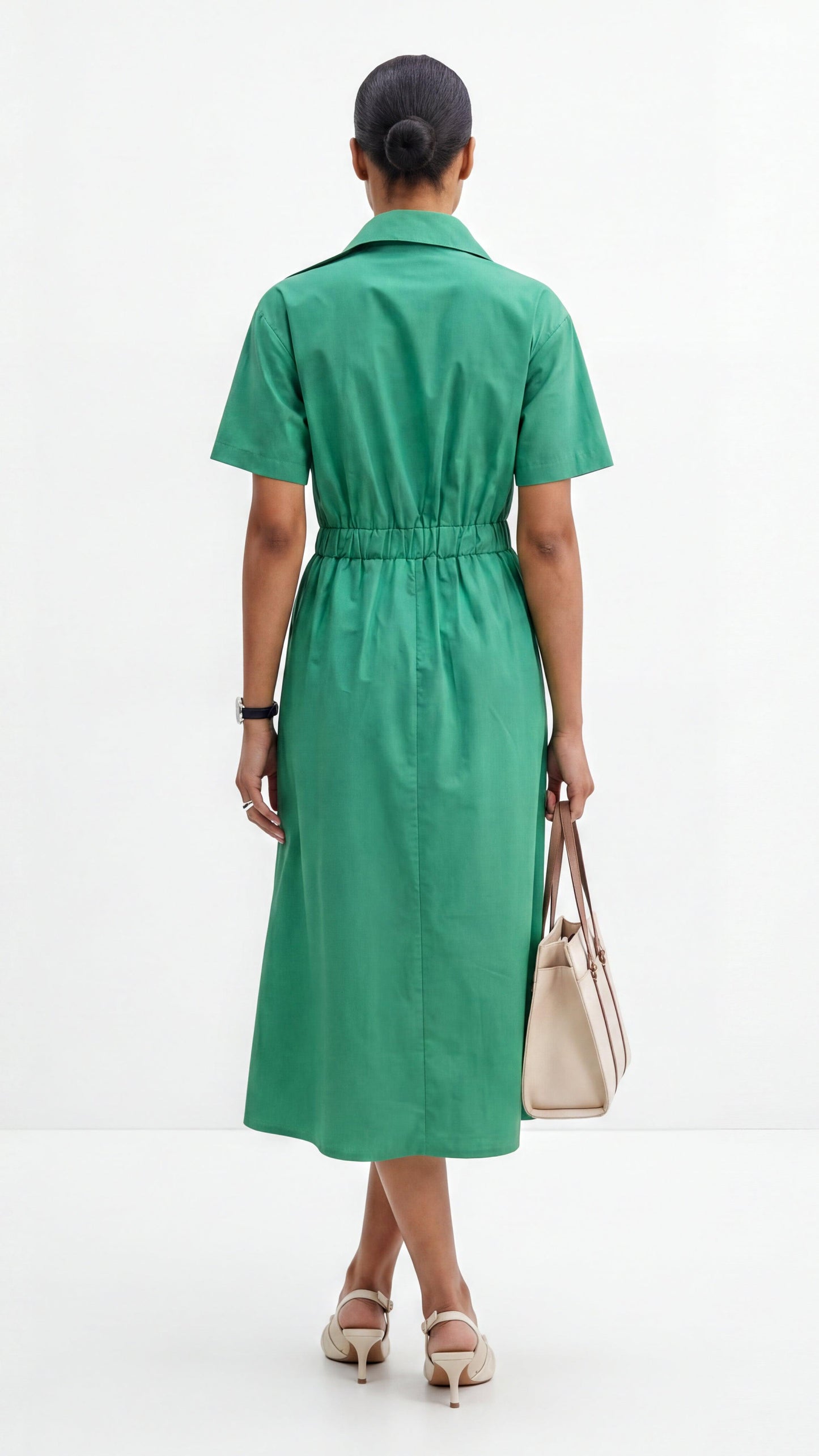 Woman wearing a green dress holding a beige handbag on a white background