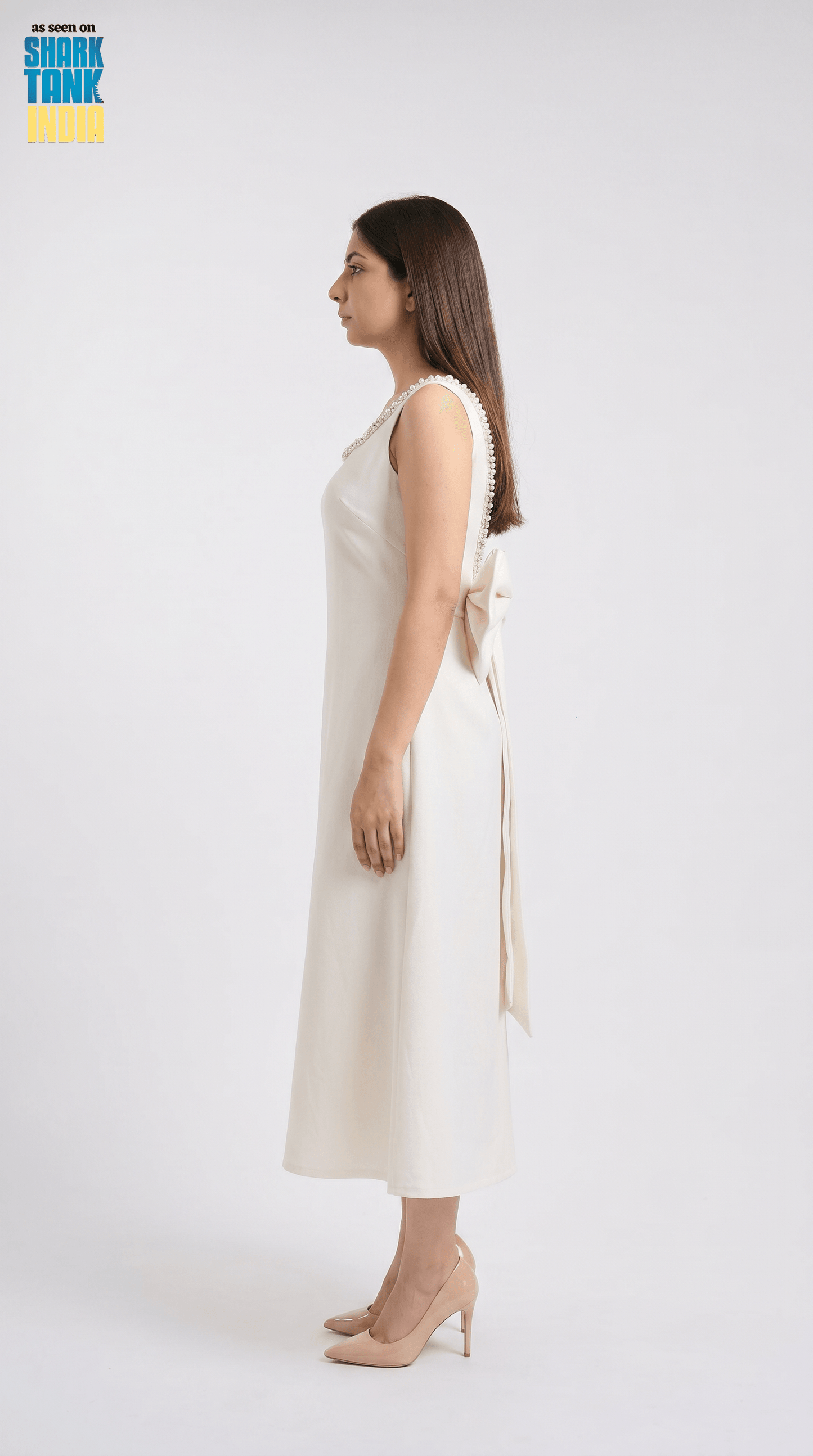 Woman wearing a white sleeveless dress with a bow detail on a white background