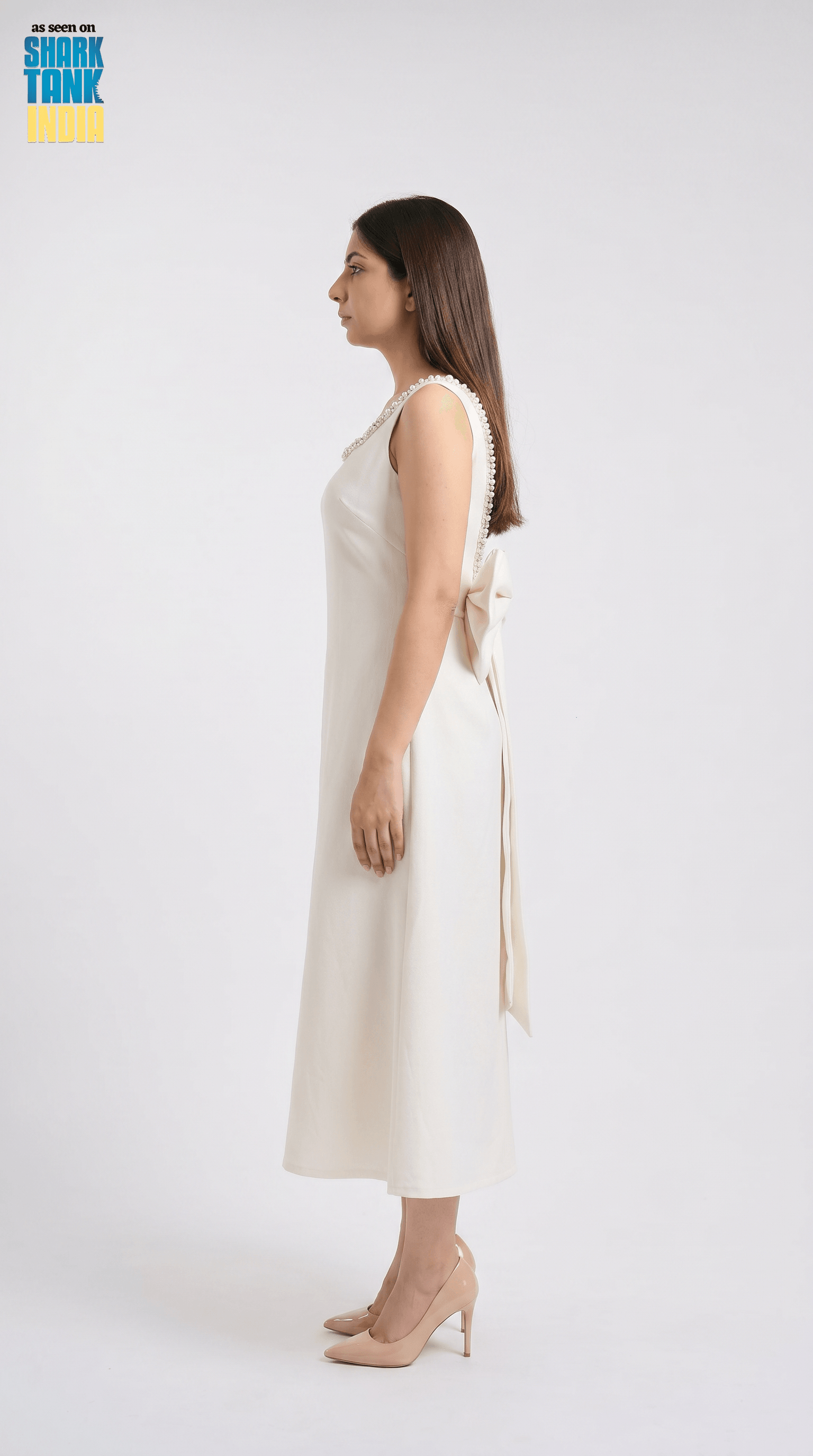 Woman wearing a white sleeveless dress with a bow detail on a white background