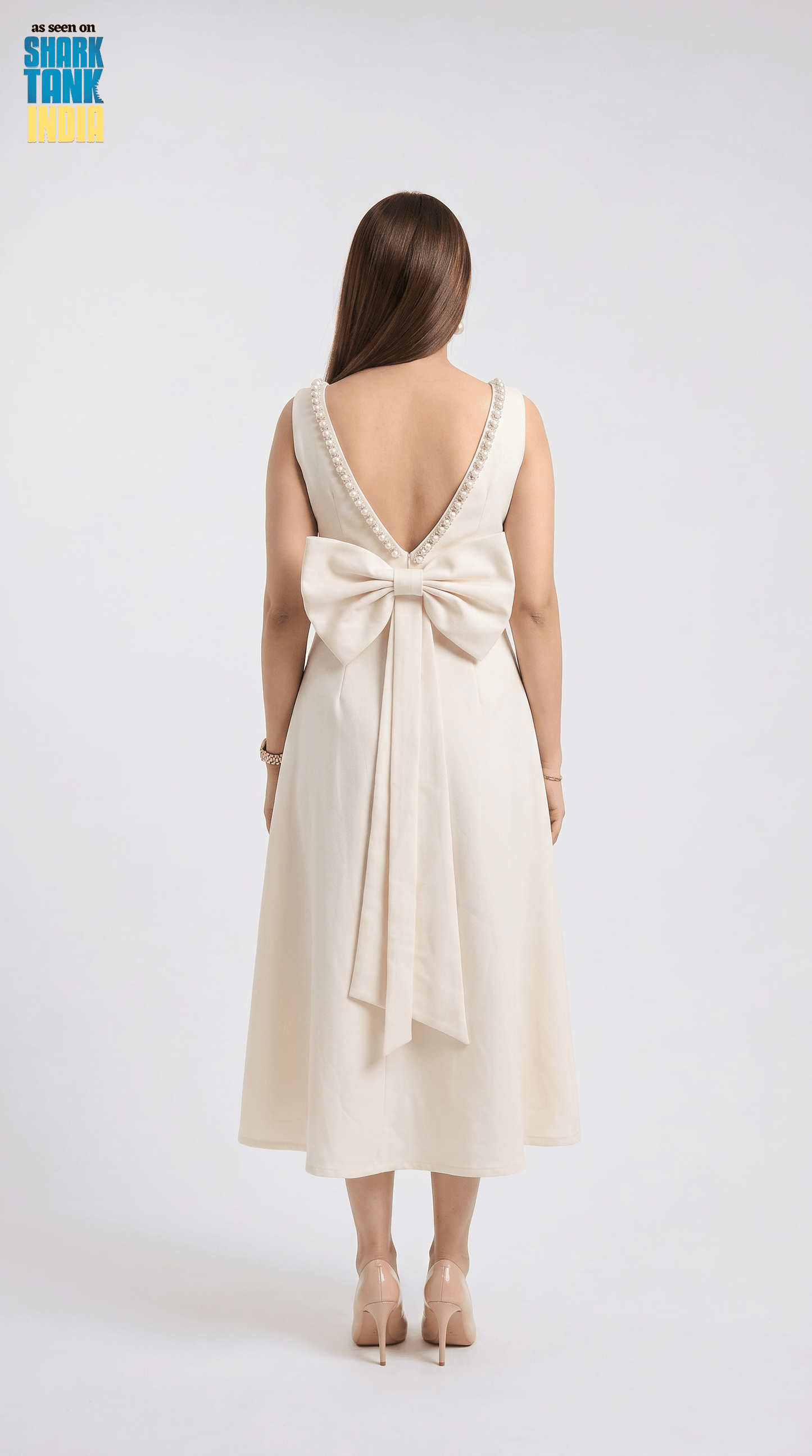 Woman wearing a cream-colored dress with a large bow detail on a white background