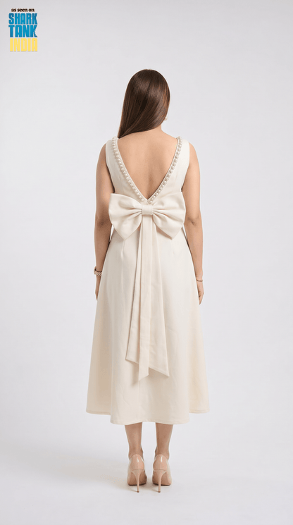 Woman wearing a cream-colored dress with a large bow detail on a white background